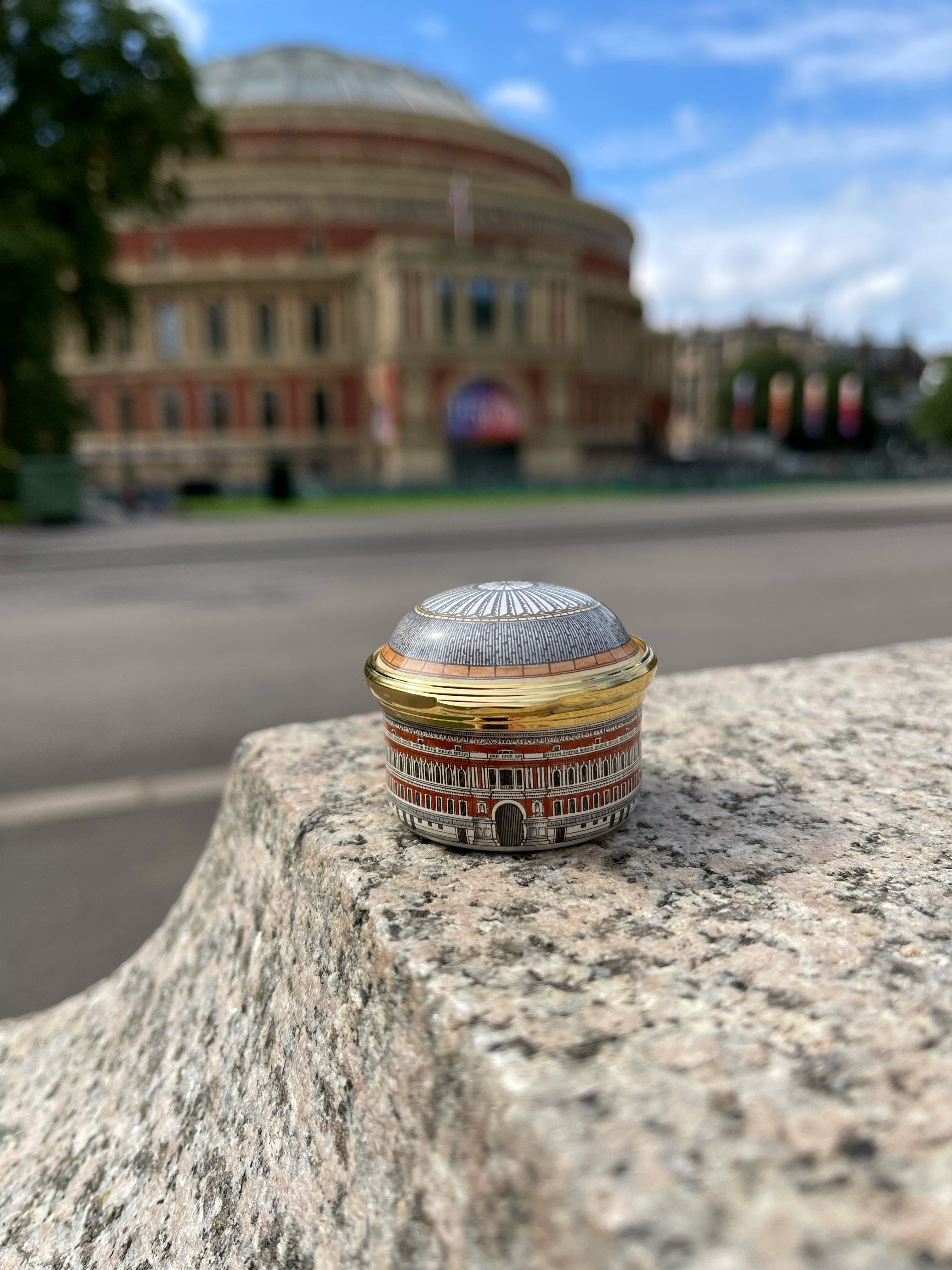 Image of Halcyon Days' Royal Albert Hall Musical enamel box sitting in front of the Royal Albert Hall